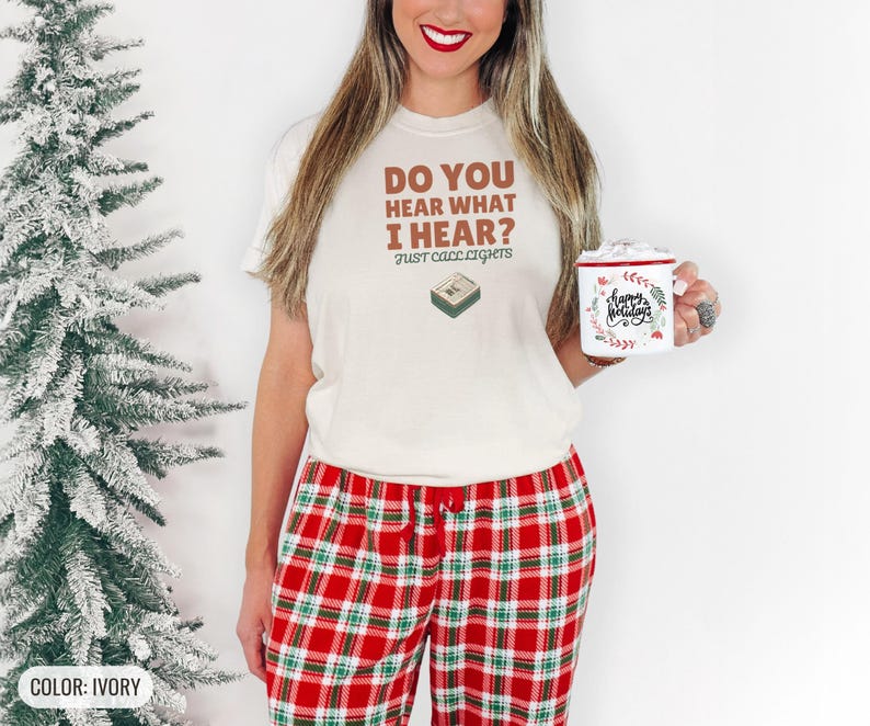 Ivory Comfort Colors t-shirt printed with the words Do You Hear What I Hear? Just Call Lights and a drawing of a rectangular electronic medical pager with a small holly sprig beside it, worn by a woman