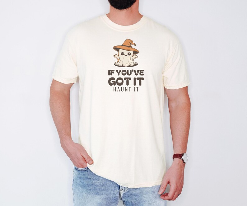 Ivory Comfort Colors t-shirt printed with the words If You'Ve Got It Haunt It and a drawing of a cute retro cartoon ghost wearing a witch hat, worn by a man