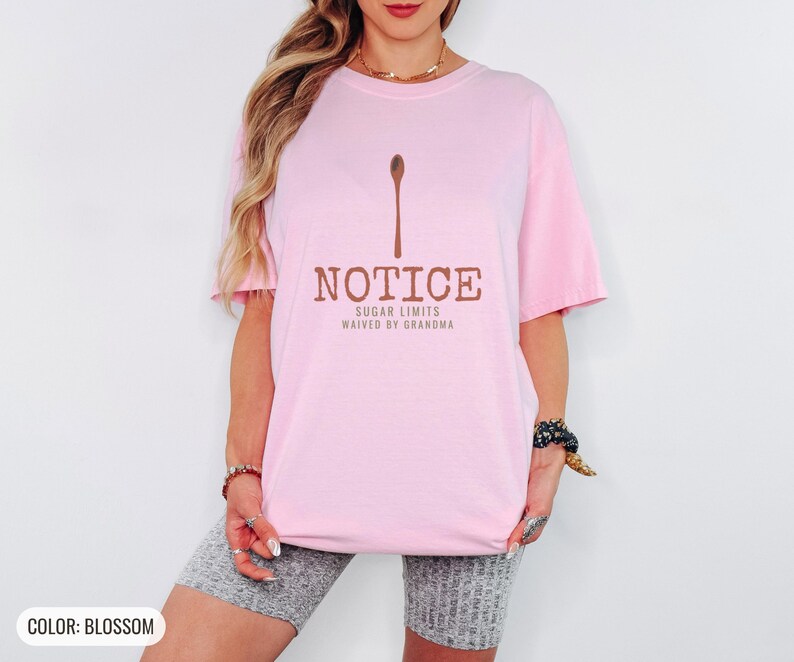 Blossom Comfort Colors t-shirt printed with the words Notice Sugar Limits Waived By Grandma and a drawing of a painted wooden spoon crossed over a cinnamon stick bundle, worn by a woman