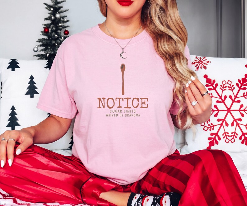 Blossom Comfort Colors t-shirt printed with the words Notice Sugar Limits Waived By Grandma and a drawing of a painted wooden spoon crossed over a cinnamon stick bundle, worn by a woman