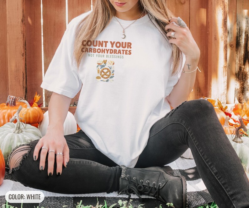 White Comfort Colors t-shirt printed with the words Count Your Carbohydrates Not Your Blessings and a drawing of a golden-brown braided pretzel with coarse salt grains, worn by a woman