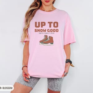Blossom Comfort Colors t-shirt printed with the words Up To Snow Good Smith Family 2026 and a drawing of a vintage metal clamp-on ice skate with red laces, worn by a woman