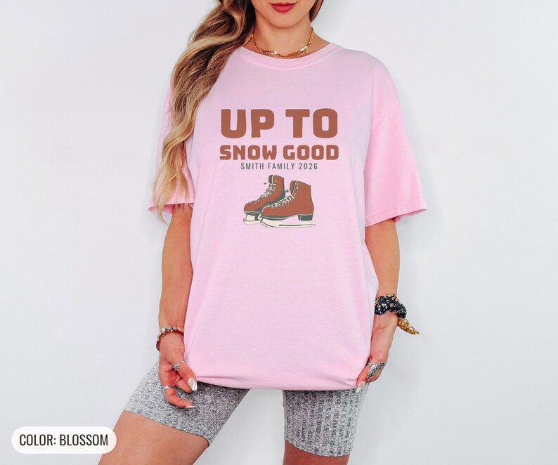 Blossom Comfort Colors t-shirt printed with the words Up To Snow Good Smith Family 2026 and a drawing of a vintage metal clamp-on ice skate with red laces, worn by a woman
