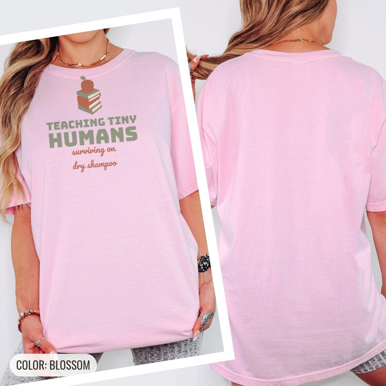 Blossom Comfort Colors t-shirt printed with the words Teaching Tiny Humans Surviving On Dry Shampoo and a drawing of a small neat stack of three closed hardcover books with PLAIN blank solid-colour spines an, worn by a woman