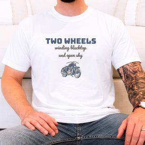 White Comfort Colors t-shirt printed with the words Two Wheels Winding Blacktop And Open Sky and a drawing of a classic cruiser motorcycle in side profile, worn by a man