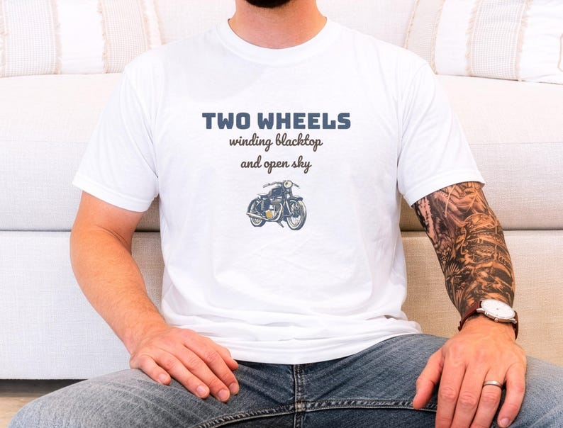 White Comfort Colors t-shirt printed with the words Two Wheels Winding Blacktop And Open Sky and a drawing of a classic cruiser motorcycle in side profile, worn by a man