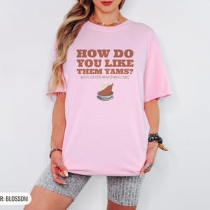 Blossom Comfort Colors t-shirt printed with the words How Do You Like Them Yams? With Extra Marshmallows and a drawing of a roasted yam sliced in half with melted marshmallow topping, worn by a woman