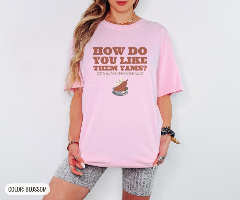 Blossom Comfort Colors t-shirt printed with the words How Do You Like Them Yams? With Extra Marshmallows and a drawing of a roasted yam sliced in half with melted marshmallow topping, worn by a woman