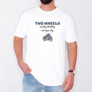 White Comfort Colors t-shirt printed with the words Two Wheels Winding Blacktop And Open Sky and a drawing of a classic cruiser motorcycle in side profile, worn by a man