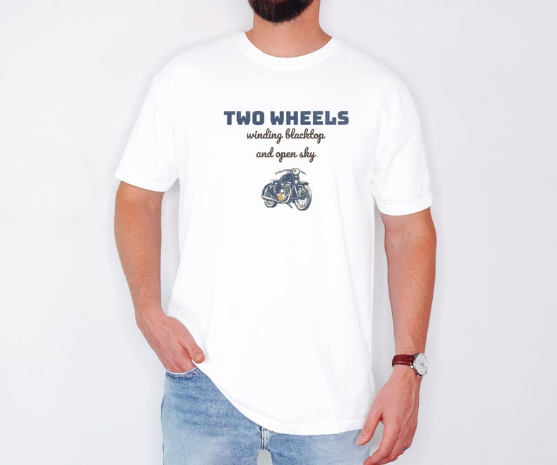White Comfort Colors t-shirt printed with the words Two Wheels Winding Blacktop And Open Sky and a drawing of a classic cruiser motorcycle in side profile, worn by a man