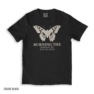 Black Comfort Colors t-shirt printed with the words Burning The Midnight Oil With The Moths and a drawing of a cecropia moth with feathery antennae, folded flat lay