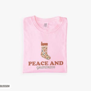 Blossom Comfort Colors t-shirt printed with the words Peace And Grandkids and a drawing of a classic knitted wool christmas stocking stuffed with small toys, folded flat lay