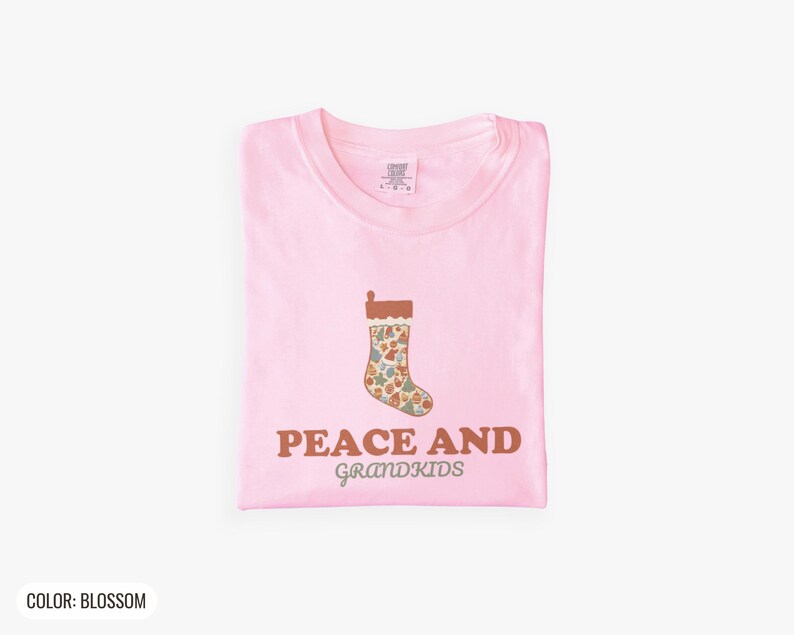 Blossom Comfort Colors t-shirt printed with the words Peace And Grandkids and a drawing of a classic knitted wool christmas stocking stuffed with small toys, folded flat lay