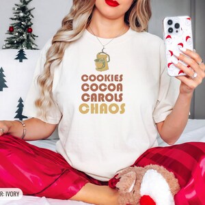 Ivory Comfort Colors t-shirt printed with the words Cookies Cocoa Carols Chaos and a drawing of a retro metal hand mixer with steel beaters, worn by a woman