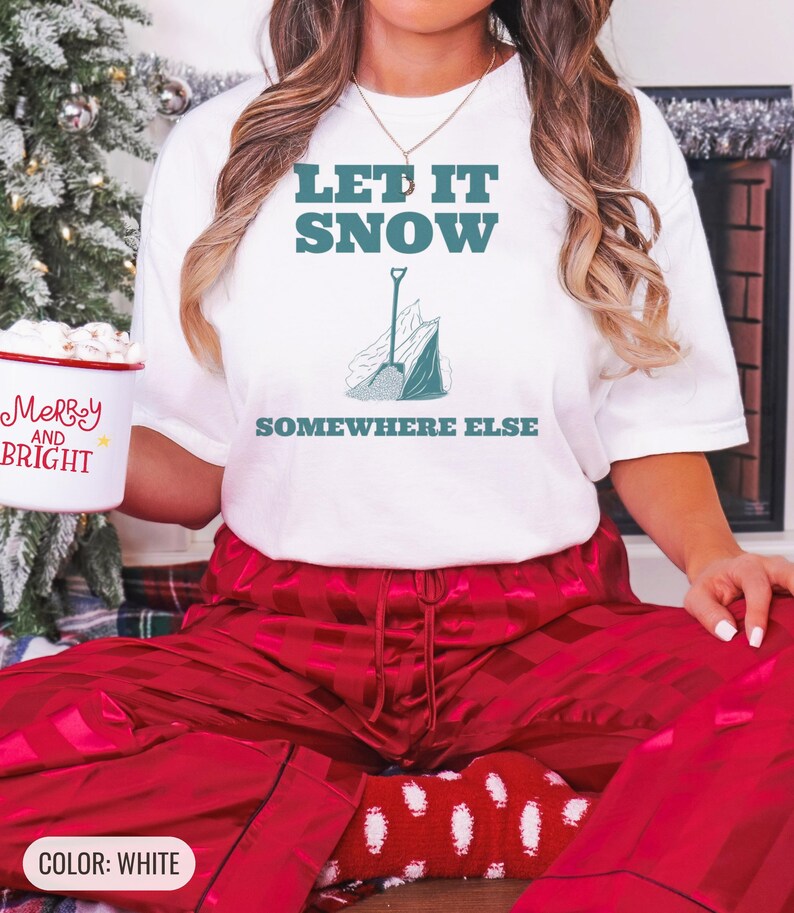 White Comfort Colors t-shirt printed with the words Let It Snow Somewhere Else and a drawing of a metal snow shovel propped beside an empty bag of rock salt, worn by a woman