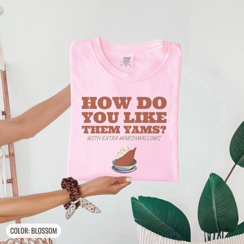 Blossom Comfort Colors t-shirt printed with the words How Do You Like Them Yams? With Extra Marshmallows and a drawing of a roasted yam sliced in half with melted marshmallow topping, folded flat lay