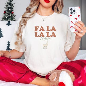 Ivory Comfort Colors t-shirt printed with the words Fa La La La Llama and a drawing of a fluffy llama, worn by a woman