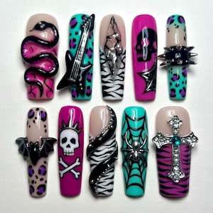 May include: A set of ten press-on nails featuring various designs including a black snake, a black electric guitar, a skull, a bat, a spider web, and a silver cross with a blue gem. The nails use a color palette of hot pink, teal, black, and white.