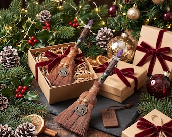 Puede incluir: Dos escobas decorativas en miniatura con cerdas marrones, cada una con una punta de cristal morado, un dije de triple luna plateado y una etiqueta de madera con la inscripción Nature's Wisdom and Sacred Protection, presentadas en cajas de regalo.