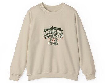 Puede incluir: Una sudadera beige de cuello redondo con texto en verde oscuro que dice "Emotionally clocked out since 9:02 AM" sobre un gráfico de un pequeño reloj analógico con ojos cerrados y manecillas rojas, con pequeñas líneas rojas.