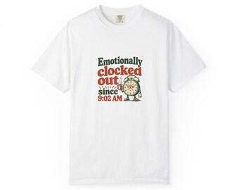 Puede incluir: Una camiseta blanca con el gráfico de un despertador con expresión cansada que sostiene una taza de café. El texto "Emotionally clocked out since 9:02 AM" aparece en letras de color verde oscuro y rojo en el centro.