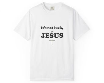Puede incluir: Una camiseta blanca de manga corta con texto negro centrado en el pecho que dice, It's not luck, it's JESUS, seguido de un símbolo de cruz negra simple. La camiseta tiene un cuello redondo y un corte estándar con una etiqueta visible.