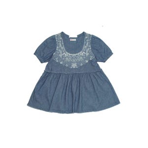 May include: A blue denim-style short-sleeve top featuring a round neckline with intricate white floral lace embroidery. The garment has a gathered waistline with a ruffled seam, short puff sleeves, and a flared silhouette that falls to the hips.