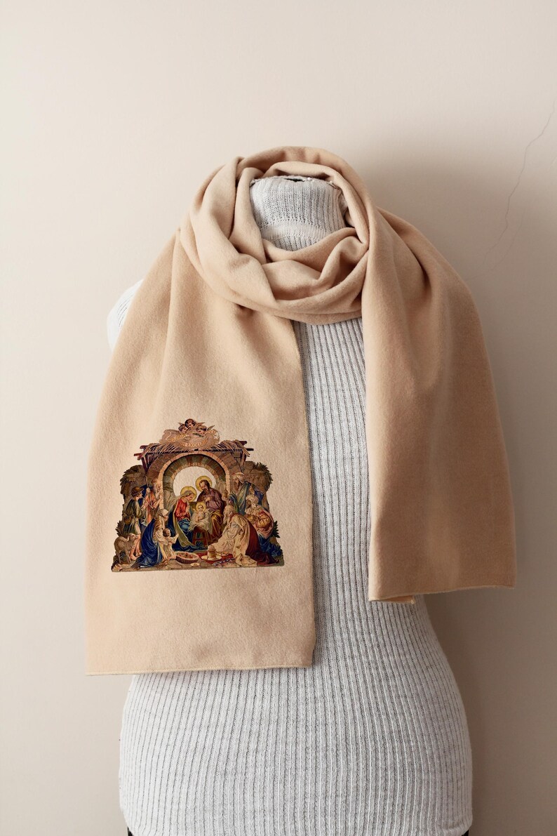 Puede incluir: Bufanda beige con una imagen religiosa detallada de la Natividad. La bufanda est&aacute; drapeada sobre un maniqu&iacute;, mostrando su longitud y textura. La imagen presenta figuras en varios colores.