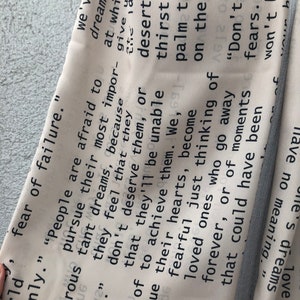 May include: A light-colored fabric with a repeating text pattern in black. The text includes phrases like "fear of failure" and "don't give fears." The fabric is folded, revealing a light blue edge.