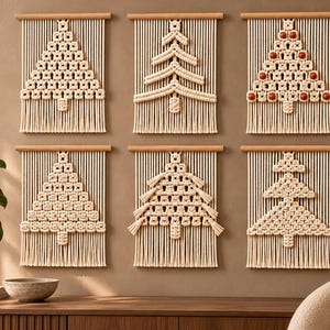 May include: Six macrame wall hangings featuring off-white cotton cord knotted into various Christmas tree shapes. Each piece is suspended from a light wooden dowel and finished with a fringed bottom edge. One design includes small red beads.