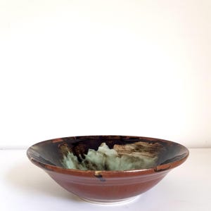 May include: A shallow ceramic bowl with a wide rim, featuring a glossy dark brown exterior and a contrasting interior glaze that blends deep espresso tones with a soft, mottled mint green centre, creating a distinct layered colour effect.