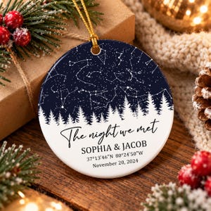 May include: A round ceramic ornament featuring a dark blue night sky with white star constellations above a white silhouette of a pine forest. The text reads: The night we met, SOPHIA & JACOB, 37°13'46"N 80°24'50"W, November 20, 2024.