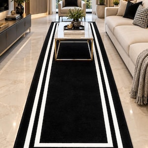 May include: A long rectangular area rug featuring a solid black center field framed by two distinct white border lines. The rug has a clean, sharp geometric design that runs the length of the floor space, providing a high-contrast visual element.