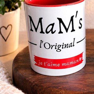 Peut inclure: Un mug en céramique blanc avec un intérieur rouge. L'avant présente le texte noir MaM's l'Original et une bannière rouge avec le texte blanc je t'aime maman accompagné d'un petit symbole de cœur blanc à la fin de la phrase.