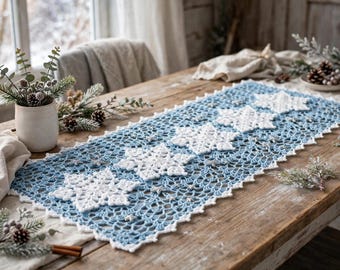 May include: A rectangular crochet table runner featuring a repeating pattern of white snowflake motifs connected by a light blue openwork mesh. The edges of the runner are finished with a scalloped border, and the design includes small silver star accents.