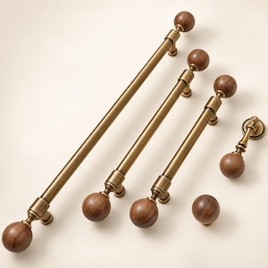 May include: A collection of cabinet hardware including three long bar pulls, one drop pull, and one round knob. Each piece features a brushed brass metal finish combined with spherical dark brown wooden accents at the ends and centers.