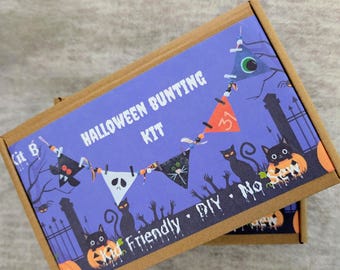 May include: A Halloween Bunting Kit in a brown cardboard box. The kit features a purple background with a bunting banner, black cats, pumpkins, and the text "Halloween Bunting Kit". The design is labeled "Kid Friendly DIY".
