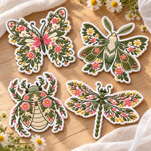 May include: Four embroidered patches featuring a butterfly, a moth, a beetle, and a dragonfly. Each insect is decorated with intricate green leaves, small white flowers, and vibrant pink blossoms, all outlined with a clean white border.
