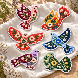 May include: Six embroidered bird patches featuring intricate floral patterns in various colors including pink, red, yellow, blue, purple, and green. Each bird is depicted with detailed wing and tail feathers adorned with small flower motifs.