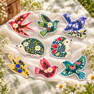 May include: A collection of eight embroidered patches featuring stylized birds and hedgehogs decorated with floral patterns. The designs include red, green, blue, yellow, and pink creatures adorned with white daisies and colorful leaves.