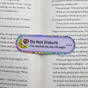 May include: A rectangular bookmark with rounded edges featuring a light purple background, a holographic crescent moon and heart icon, and the black text "Do Not Disturb" followed by "I've reached the last 100 pages" and three dots.