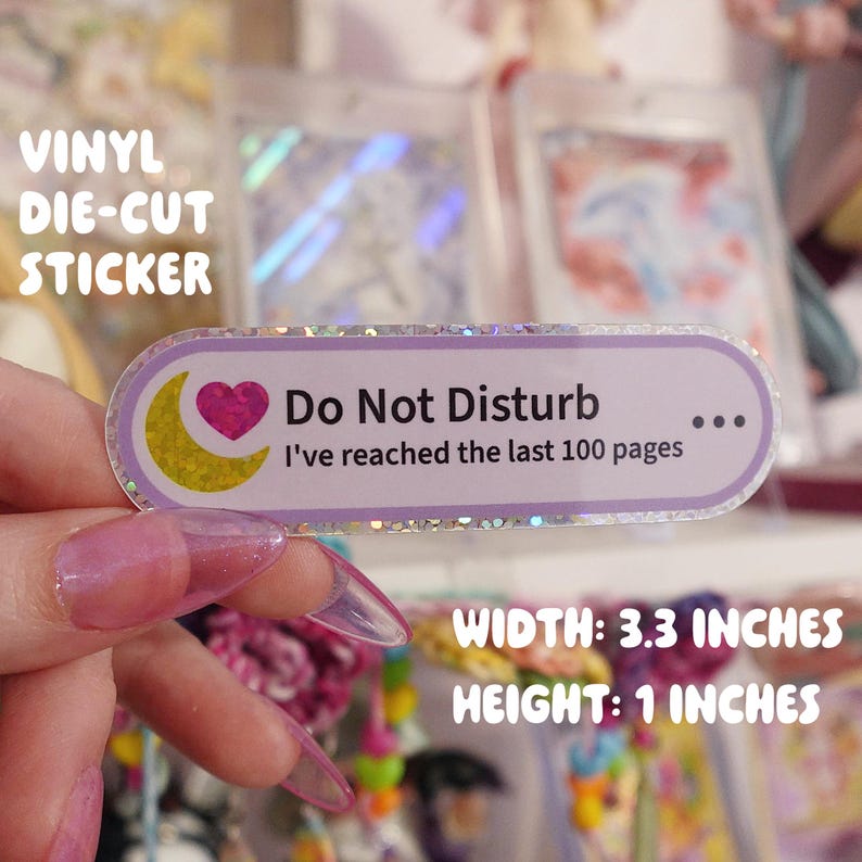 May include: A rectangular vinyl die-cut sticker with rounded edges, featuring a purple border and a glittery finish. It displays a yellow crescent moon, a pink heart, and the text: Do Not Disturb, I've reached the last 100 pages. It is 8.38 cm wide and 2.54 cm high.