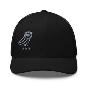Peut inclure: Une casquette de type trucker noire avec un panneau arrière en filet et un panneau avant plein. Sur le côté avant gauche est brodé le contour gris clair d'un hibou, placé juste au-dessus des lettres AMA, également cousues en fil gris clair.