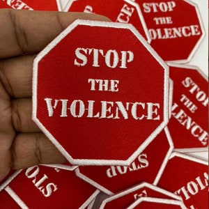 May include: A stack of red stop sign shaped patches with white stitching. The patches say "Stop the Violence" in white text.