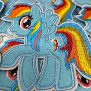 May include: A stack of blue, yellow, orange, and red embroidered patches featuring a cartoon pony with a rainbow tail.