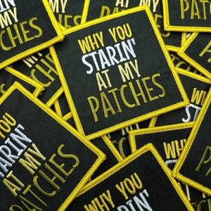 May include: A close-up of several black fabric patches with yellow stitching. The patches have the text "Why you starin' at my patches" in white and gold lettering.