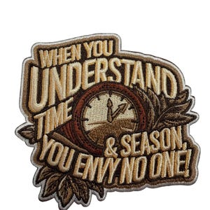 Puede incluir: Un parche bordado que presenta una esfera de reloj central rodeada de hojas estilizadas. El texto dice: WHEN YOU UNDERSTAND TIME & SEASON, YOU ENVY NO ONE! El diseño utiliza tonos marrones, beige y crema con un borde oscuro sobre fondo blanco.