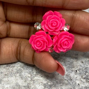 Op de afbeelding: Drie roze roosvormige versieringen met heldere strasssteentjes. De versieringen zijn bij elkaar gegroepeerd en lijken van plastic te zijn.