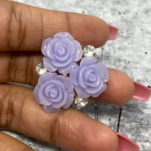 Op de afbeelding: Een cluster van drie lavendelkleurige harsrozen met strassaccenten. De rozen zijn in een cluster gerangschikt en zijn bevestigd aan een gouden metalen basis.