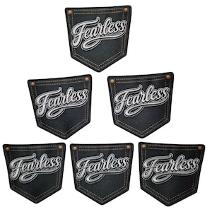 Puede incluir: Un conjunto de seis parches de tela gris carbón oscuro con forma de bolsillos de pantalón, cada uno con la palabra Fearless bordada en letras cursivas blancas con borde negro, acentuados por dos pequeños remaches de color cobre.